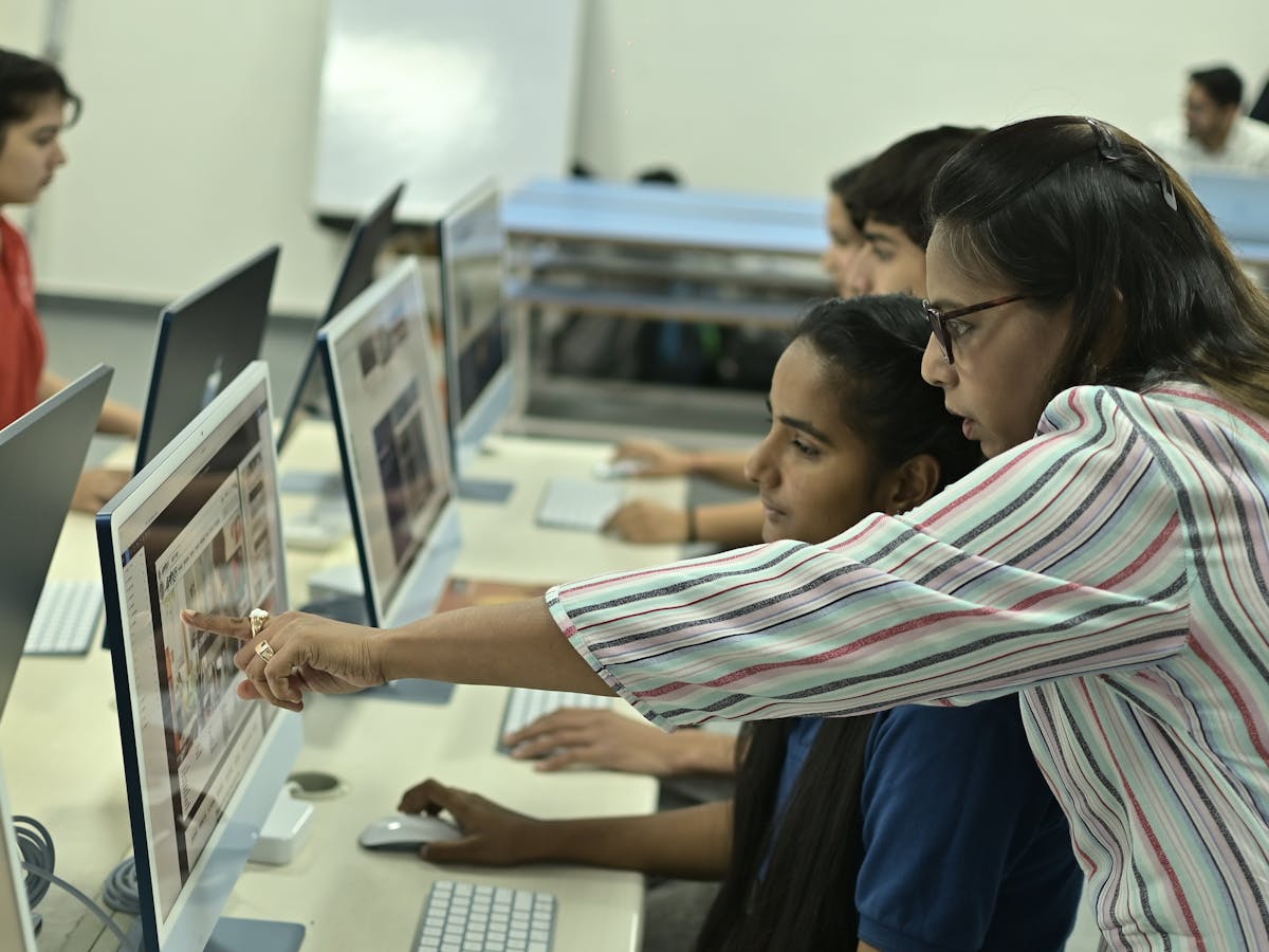 Teacher guiding an Indian student at a computer in a digital classroom